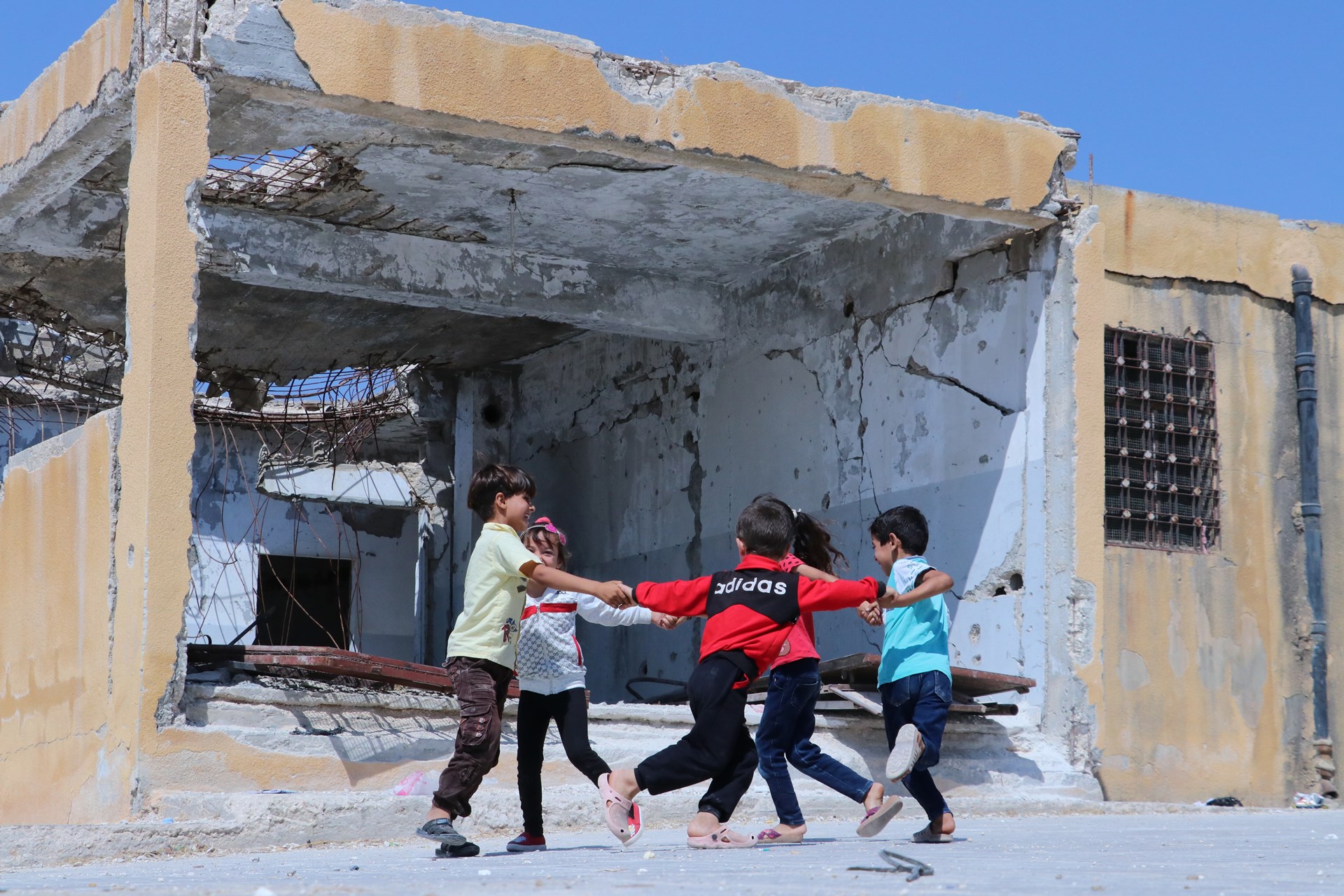 Barn leker utenfor ruinene av skolen sin i Syria. Foto.