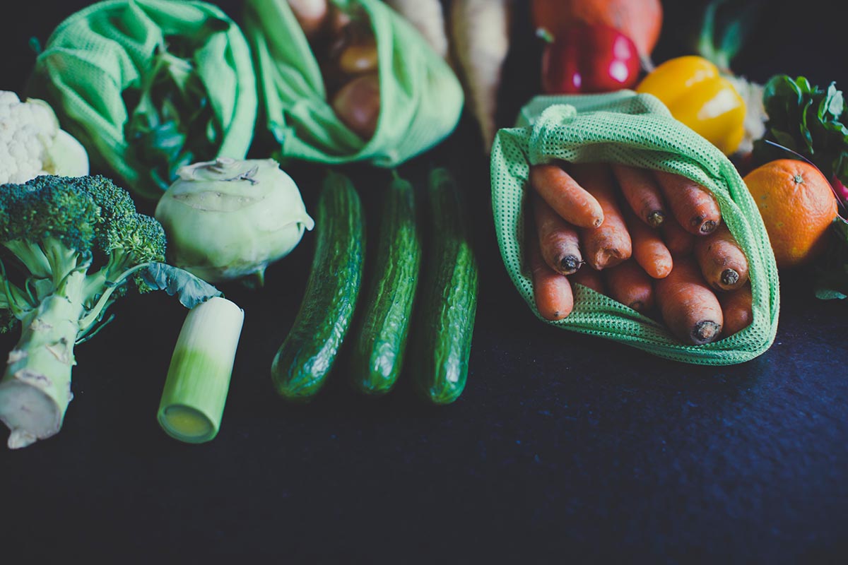 Et utvalg grønnsaker; gulrøtter, brokkoli, agurk; ligger på en sort bordplate. Foto.