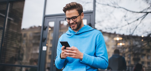 En mann kledd i en blå hettegenser ser på telefonen sin og smiler