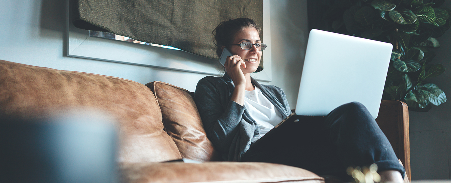 En kvinne sitter smilende i en brun skinnsofa med PC på fanget