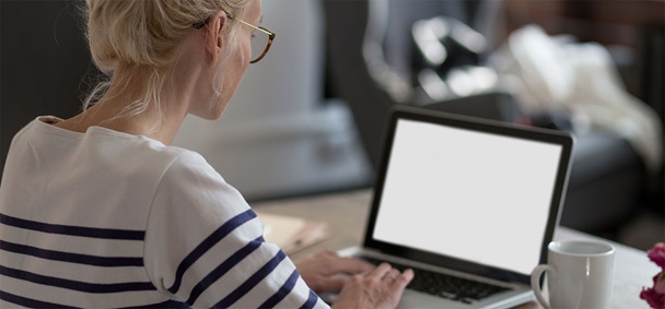 Ung kvinne med hestehale og briller sitter foran et bord med en bærbar PC og en kaffekopp