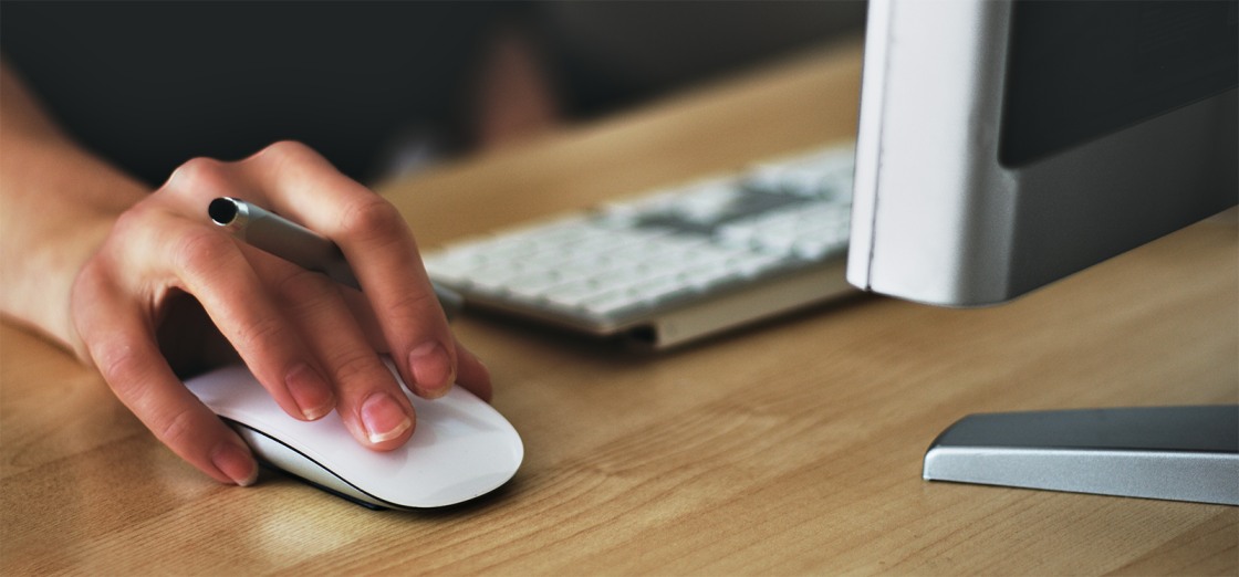 Hånd beveger en datamus på et skrivebord omgitt av tastatur og en PC-skjerm