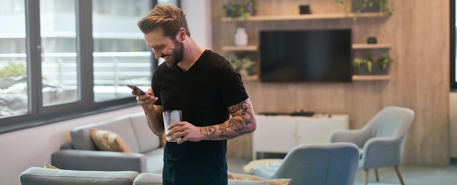 En ung mann kikker smilende på mobilen hans inne på et møterom