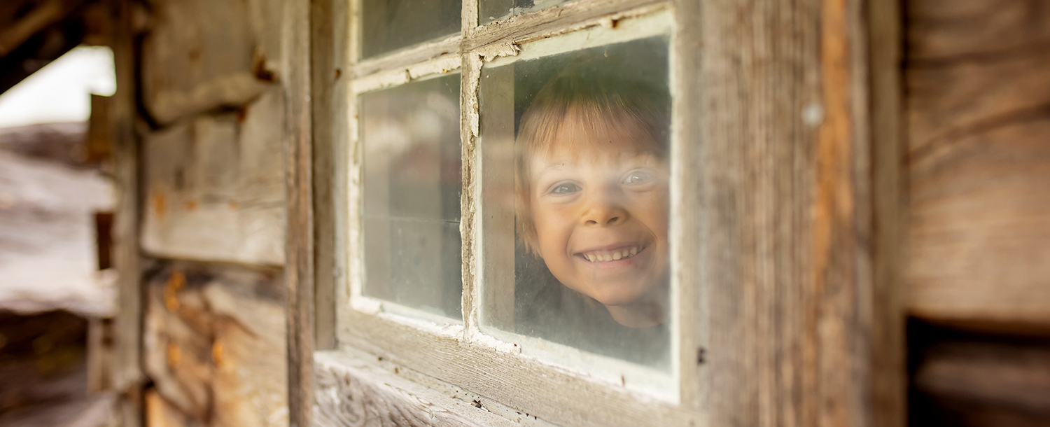 Et gammelt hus, muligens fra et museum. Gjennom vinduet i bygningen kan man se en liten gutt som smiler.