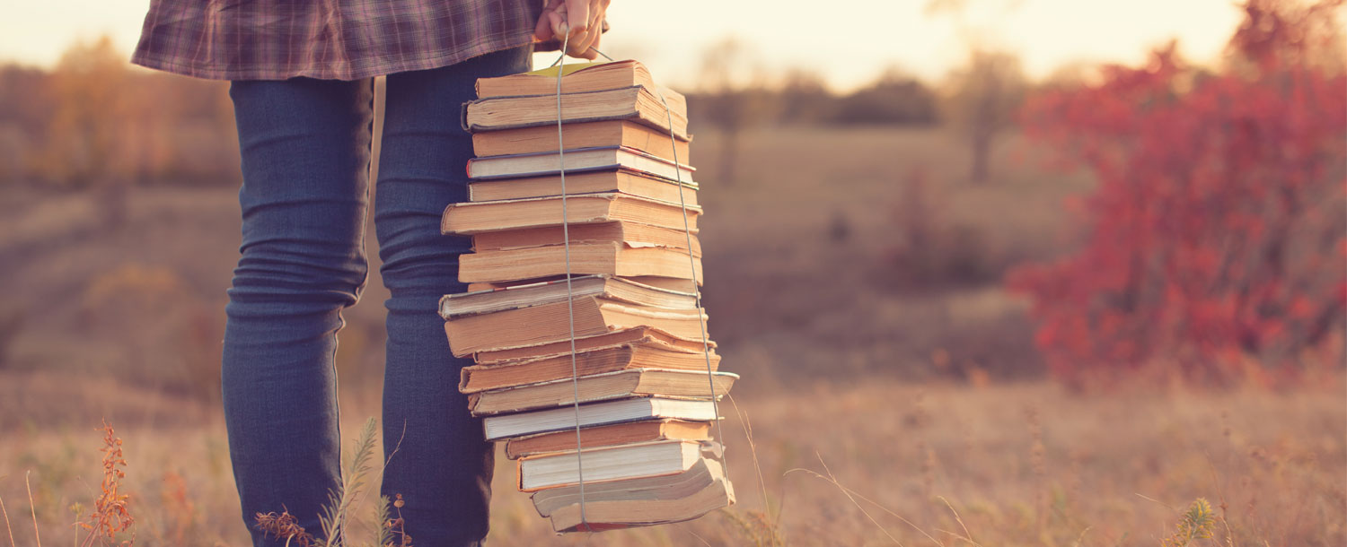 En jente holder flere bøker i den armen. Bøken har et nøste festet rundt seg. 