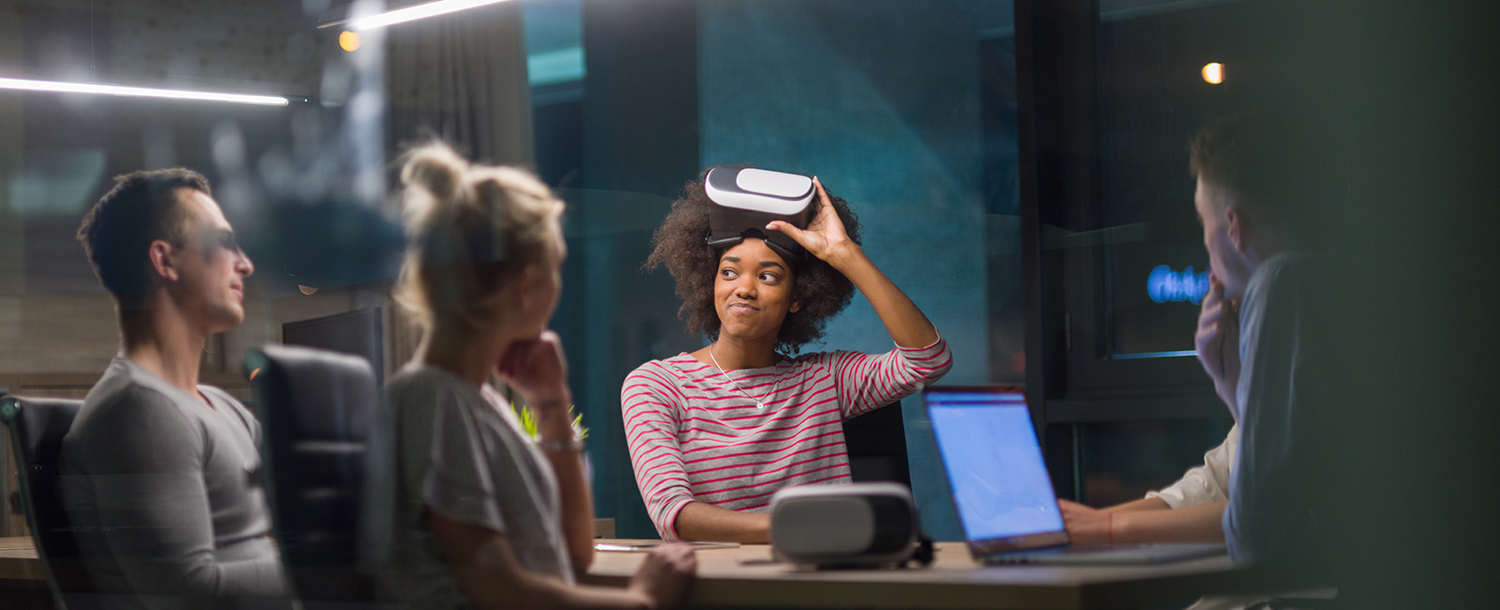 Fire mennesker sitter rundt et møtebord. En kvinne drar VR-briller vekk fra øyne. 