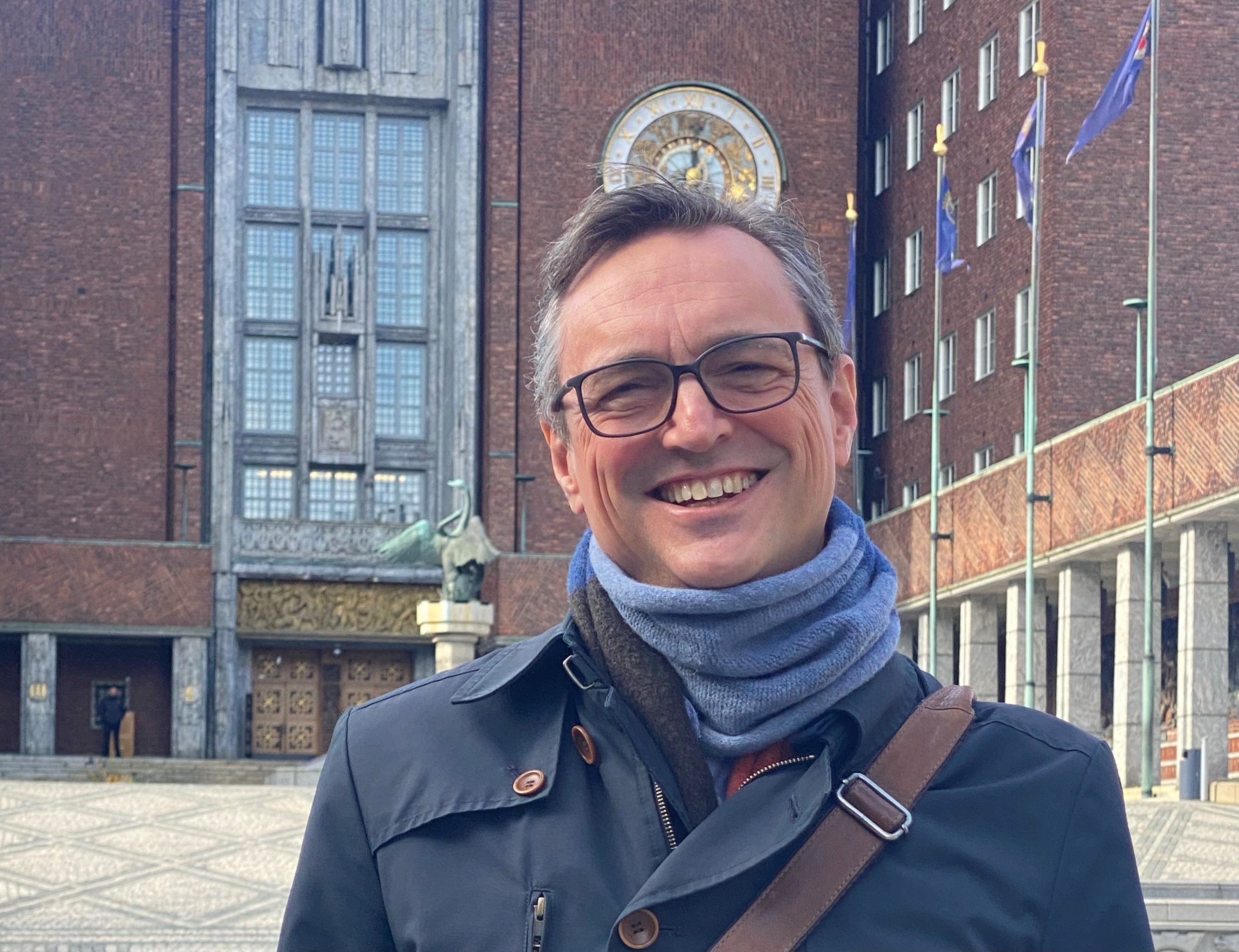Julius Okkenhaug står foran rådhuset i Oslo og smiler til kamera